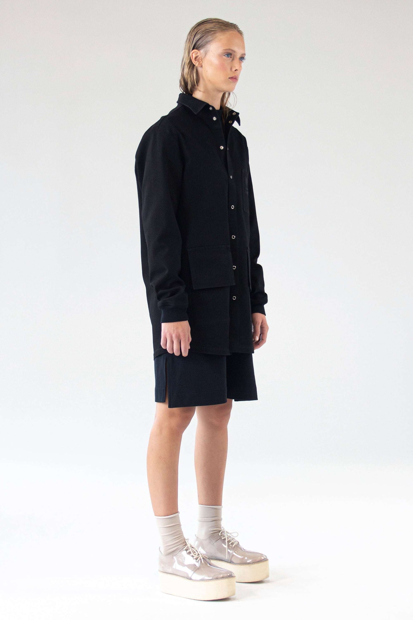 Model wearing One Wolf Unisex Denim Jacket Shirt Desire in black, side view, long silhouette with utility pockets